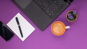 Ordinateur portable sur un fond violet avec un café et un bloc note